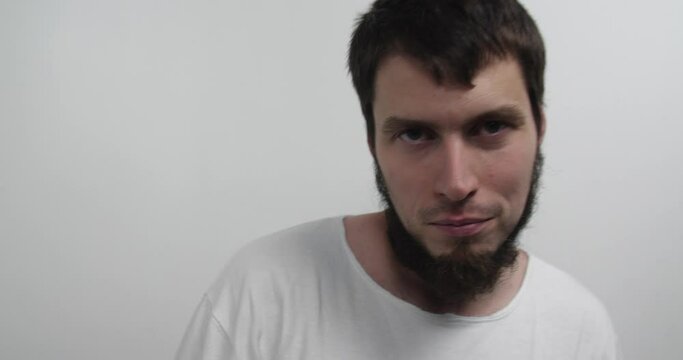 Close-up of the face of a violent psychiatric patient. Young caucasian man  in straitjacket with beard, dark hair and insane smile looking at the camera in white ward of asulym, spitting out pills