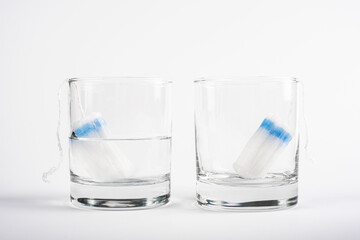 two tampons for menstruation in a glass cup with and without water on white background tampon absorbency test close-up