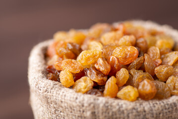 Close up shot of raisins in sack. Raisins made of grape in linen bag against dark background