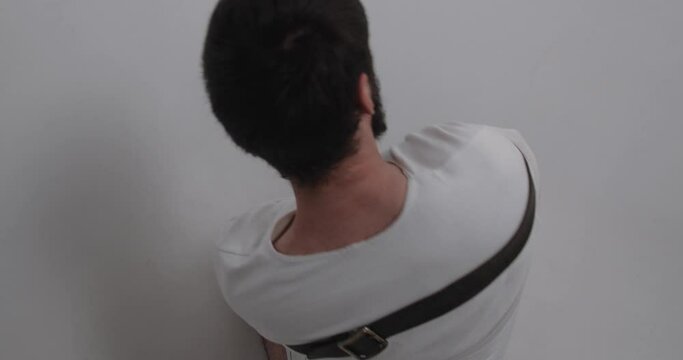 Rear view of unrecognizable psychiatric patient. Young caucasian man  sitting on floor trying to free from straitjacket in white ward of asulym. Treatment of schizophrenia in psychiatric clinic