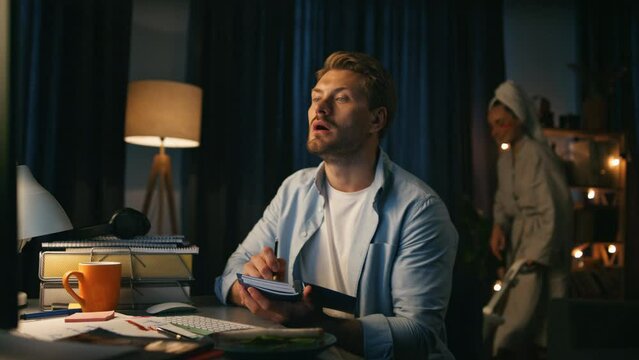 Focused man writing remarks at home closeup. Woman dancing vacuuming at evening
