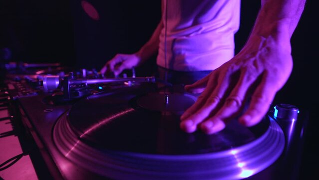 Hip hop dj scratches vinyl record on turn table player. Disc jockey scratching records on turntables in night club