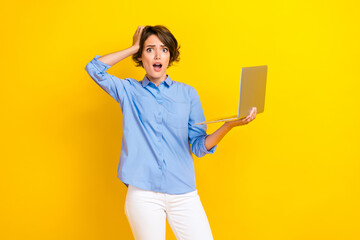 Fototapeta premium Photo of adorable pretty terrified girl with bob hairdo dressed blue shirt hold laptop hand on head isolated on yellow color background