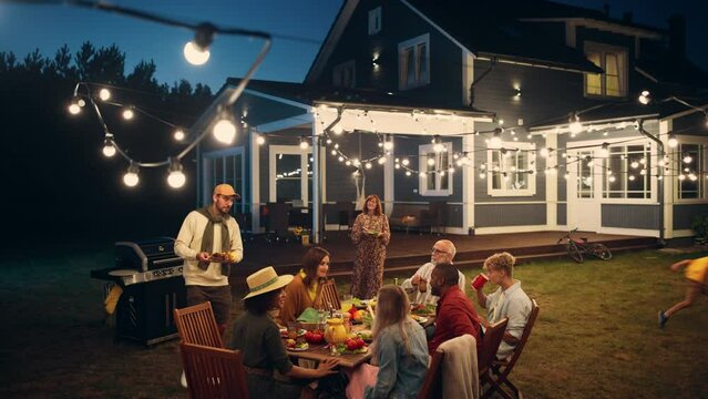 Group of Multiethnic Diverse People Having Fun, Communicating with Each Other and Eating at Outdoors Dinner. Family and Friends Gathered Outside Their Home on a Warm Summer Evening.