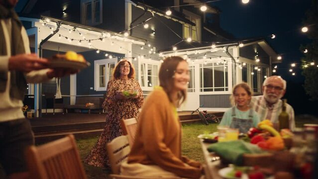 Big Family Garden Night Party Celebration, Gathered Together at a Table with Relatives and Friends. Young and Senior People are Eating, Drinking, Passing Dishes, Joking and Having Fun.