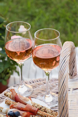 Glasses of delicious rose wine and food on picnic basket outdoors