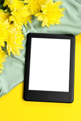 Modern e-book reader and flowers on yellow background, flat lay