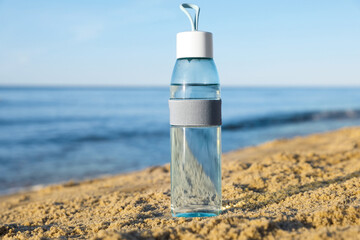 Glass bottle with water on wet sand near sea