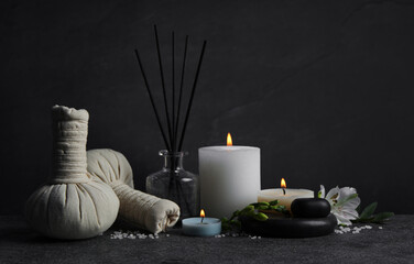Beautiful spa composition with different care products and burning candles on dark grey table against black background. Space for text