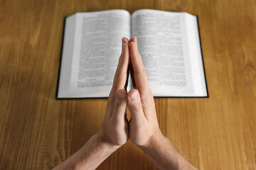 Man with Bible praying at wooden table, closeup