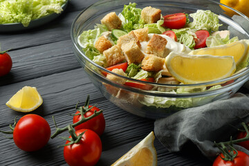 Bowl of delicious salad with Chinese cabbage, lemon, tomatoes and bread croutons on black wooden table, closeup