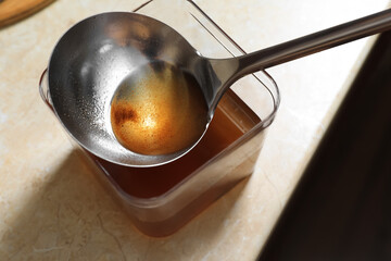 Container and ladle with used cooking oil on beige table