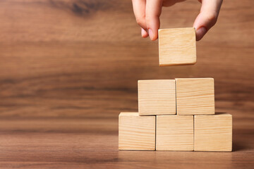 Woman building pyramid of cubes on wooden background, closeup with space for text. Idea concept