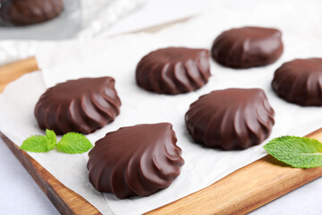 Delicious chocolate covered zephyrs and mint on wooden board, closeup
