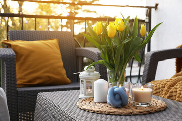 Soft pillow, blanket, burning candles and yellow tulips on rattan garden furniture outdoors