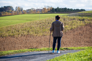 Lady nordic walking style stands on a countryside roadand watches the view