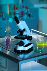 Modern microscope and glassware with colorful liquids on metal table in laboratory