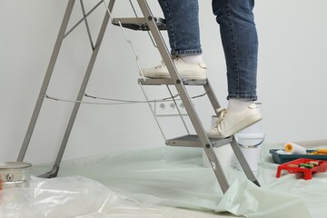 Woman standing on metallic folding ladder and painting tools, closeup