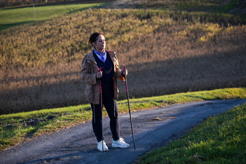Elder lady nordic walking on a countryside road and watching landscape