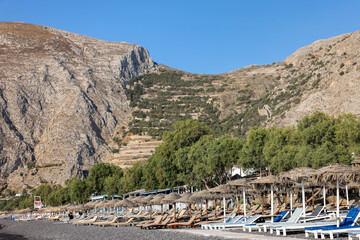 : Sun loungers on the black volcanic beach of Kamari in Santorini. Cyclades, Greece