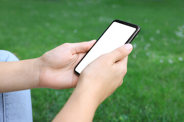 Woman using smartphone on green grass outdoors, closeup