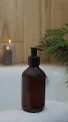 Black bottle of bubble bath and candles on tub indoors