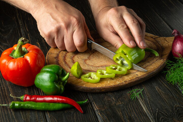 The cook cuts green peppers on a cutting board to prepare a vitamin salad. Delicious peasant food