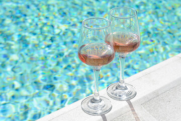 Glasses of tasty rose wine on swimming pool edge