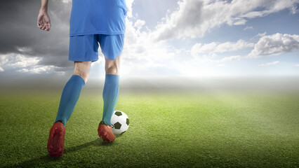 Rear view of a football player man in a blue jersey dribbling the ball
