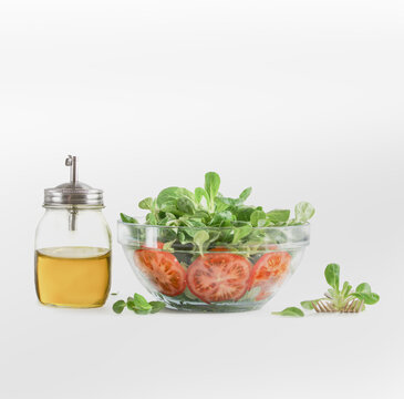 Fresh green salad in glass bowl with olive oil bottle on white background. Healthy food and dieting concept