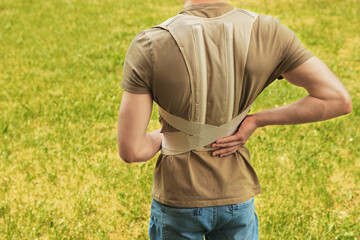 Closeup of man with orthopedic corset on green grass outdoors, back view