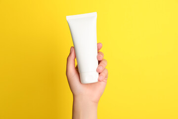 Woman holding tube of face cream on yellow background, closeup