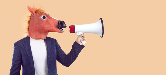Man in trendy rubber horse mask makes announcement or advertises using megaphone. Creative concept for advertising. Man with animal head speaks into loudspeaker near copy space on beige background.