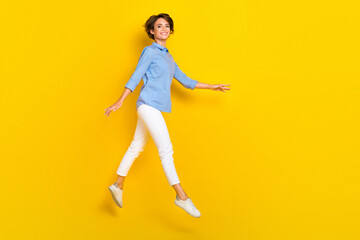 Fototapeta na wymiar Full length photo of sweet adorable girl dressed blue shirt jumping high walking empty space isolated yellow color background
