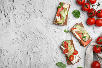 Tasty rye crispbreads with salmon, cream cheese and vegetables on grey textured table, flat lay. Space for text