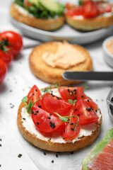 Tasty rusk with cream cheese, fresh tomatoes and black sesame seeds on white table, closeup