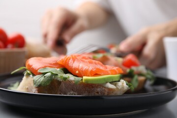 Tasty bruschetta with salmon, arugula and avocado on black plate, closeup