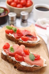 Tasty bruschettas with prosciutto, tomatoes and cheese on white wooden table, closeup