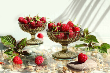  Ripe raspberries in small vases against a white wall with a shadow from objects