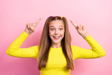 Portrait of impressed ecstatic girl with ponytails dressed yellow long sleeve directing empty space isolated on yellow color background