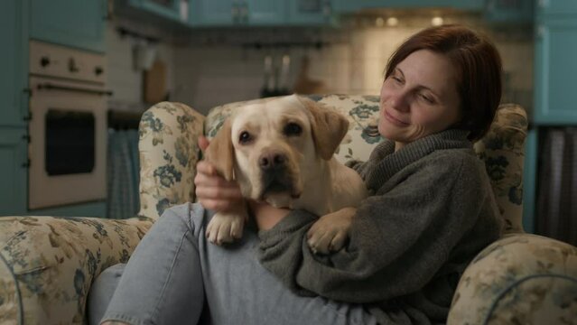 Woman petting pet dog at home. Labrador Retriever dog and its owner are having fun together sitting on couch.