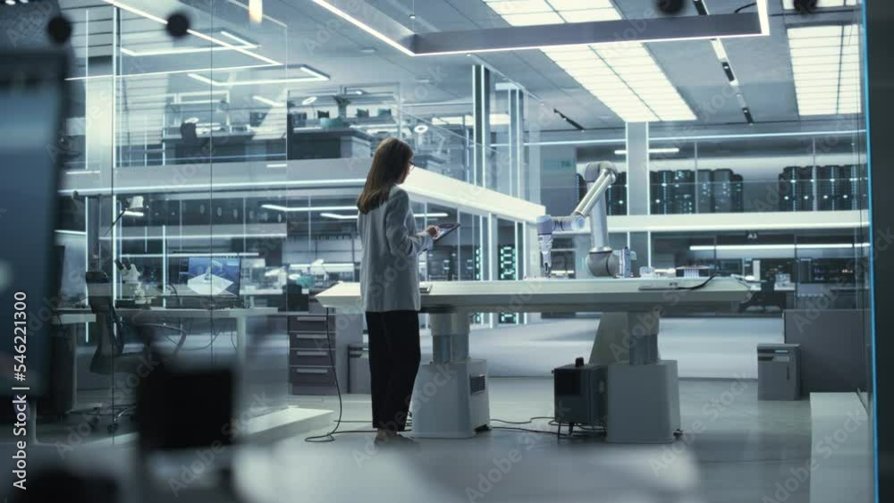 Fototapete Industrial Robotics Engineer Comes to a Table With Robotic Arm in a High Tech Factory. Female Scientist Uses Tablet Computer to Manipulate and Program the Robot to Pick Up and Move a Metal Component.