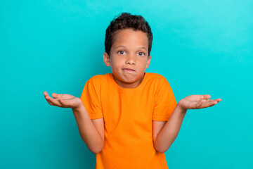 Photo of doubtful funny little guy dressed orange t-shirt shrugging shoulders isolated teal color...