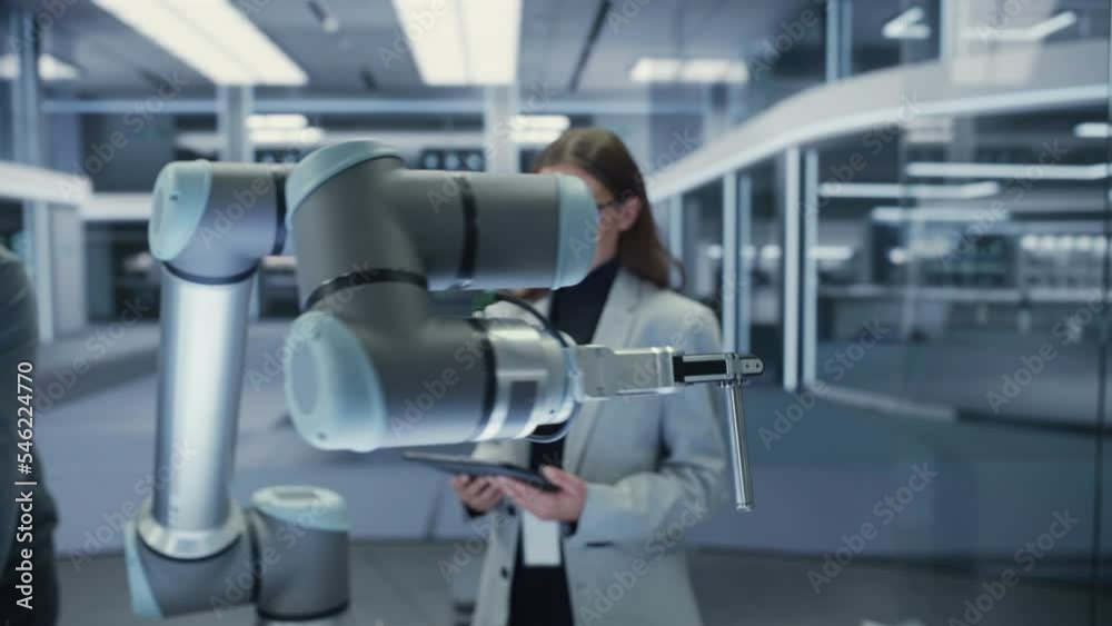 Poster Close Up Following Footage of a Modern Robotic Arm Holding and Moving a Mechanical Metal Component. Diverse Team of Engineers Using Tablet Computer to Manipulate and Program the Robot.