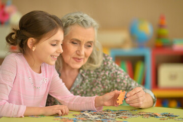 Fototapeta premium Grandmother with little granddaughter collecting puzzle