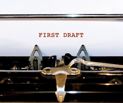 Vintage typewriter with white blank paper typed FIRST DRAFT, concept of a rough draft or very first version of of writing piece - sketch of what writing work will be like