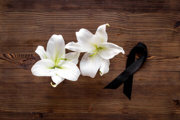 Fototapeta na wymiar White liles flowers and black ribbon as symbol of the funeral. Mourning concept