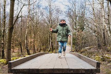 Careless child jumping or leaping on a wooden trampoline in the woods engaging in a funny outdoor activity. Lighthearted kid hopping on a timbered board or launching pad among bare trees in a forest