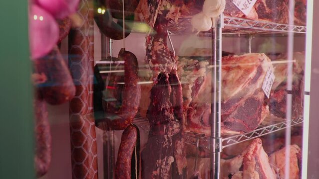 Slices of dried beef meat along with types of sausages in dry ading cabinet. Dry-aged cuts of raw meat. Food manufactoring.
