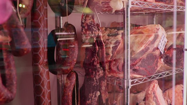 Slices of dried or smoked beef meat along with types of sausages in dry ading cabinet. Dry-aged cuts of raw meat. Food manufactoring.